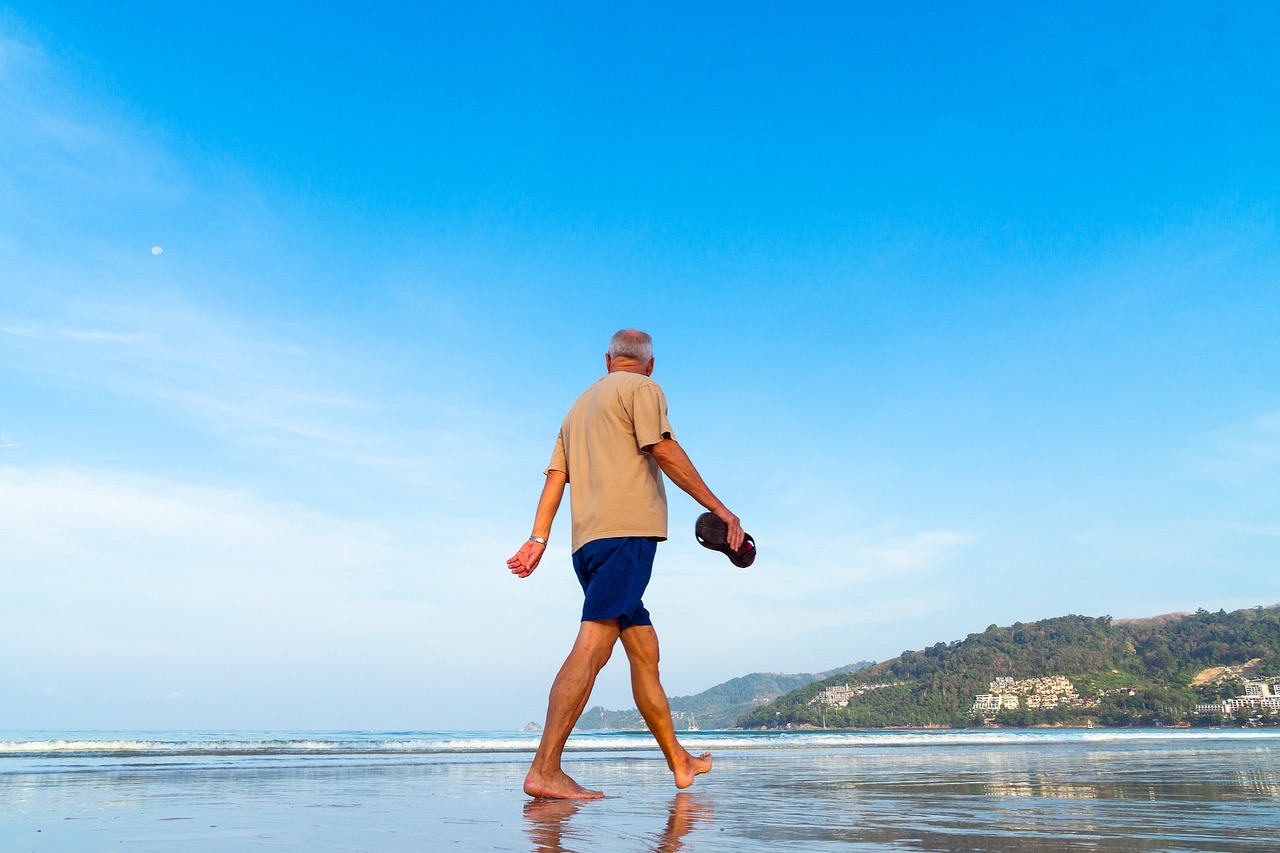 A senior man walking barefoot along a beach
